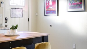 A dining area with a wooden table, two yellow chairs, a potted plant, and two framed posters on the wall.