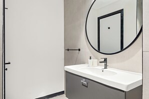 A modern bathroom with a white sink, a round mirror, and a towel dispenser. - Silkhaus 15 Northside, Business Bay Dubai (Dubai)