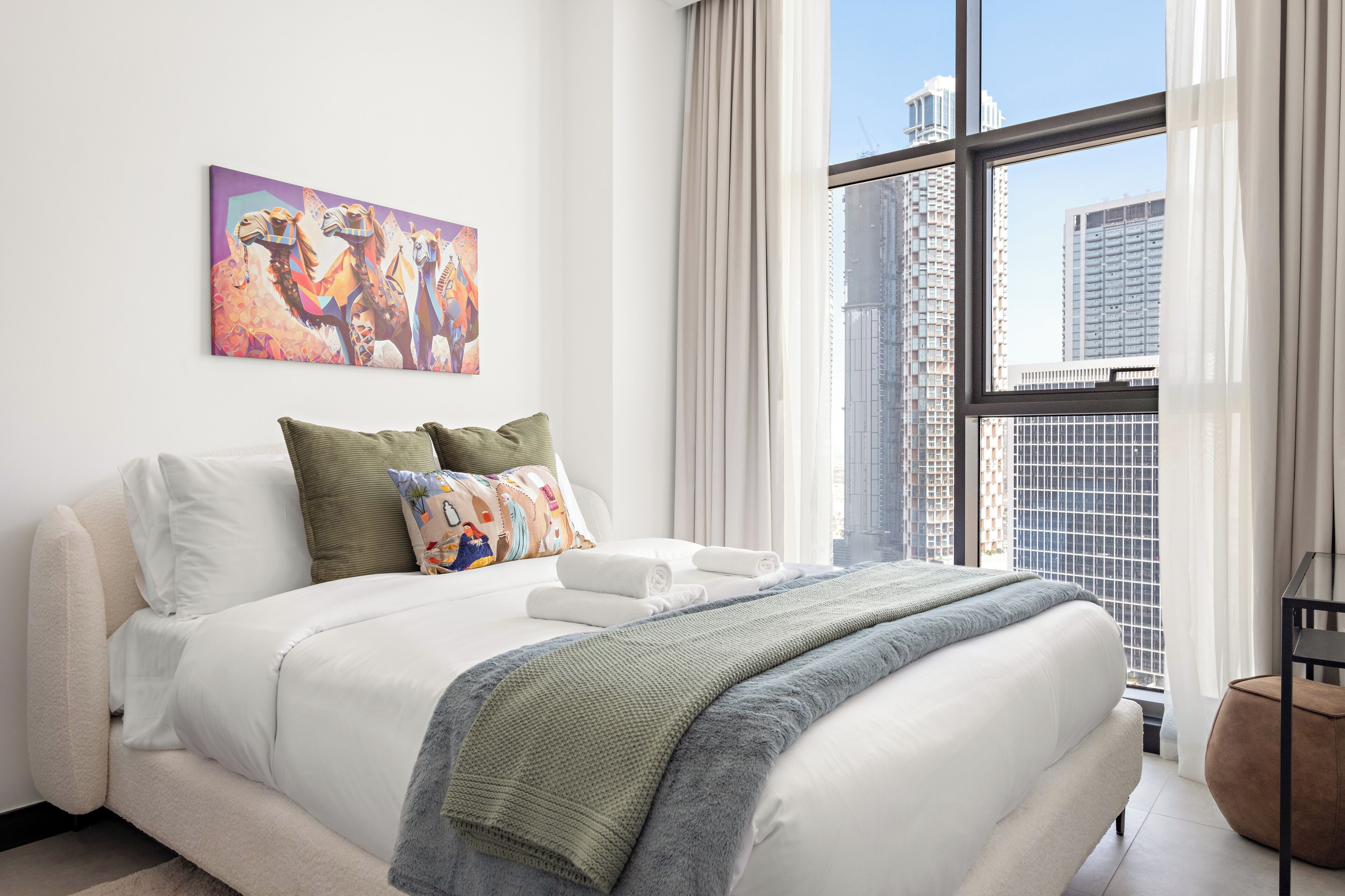 Une chambre d’hôtel moderne avec un grand lit, une vue sur la ville et une œuvre d’art colorée accrochée au mur.