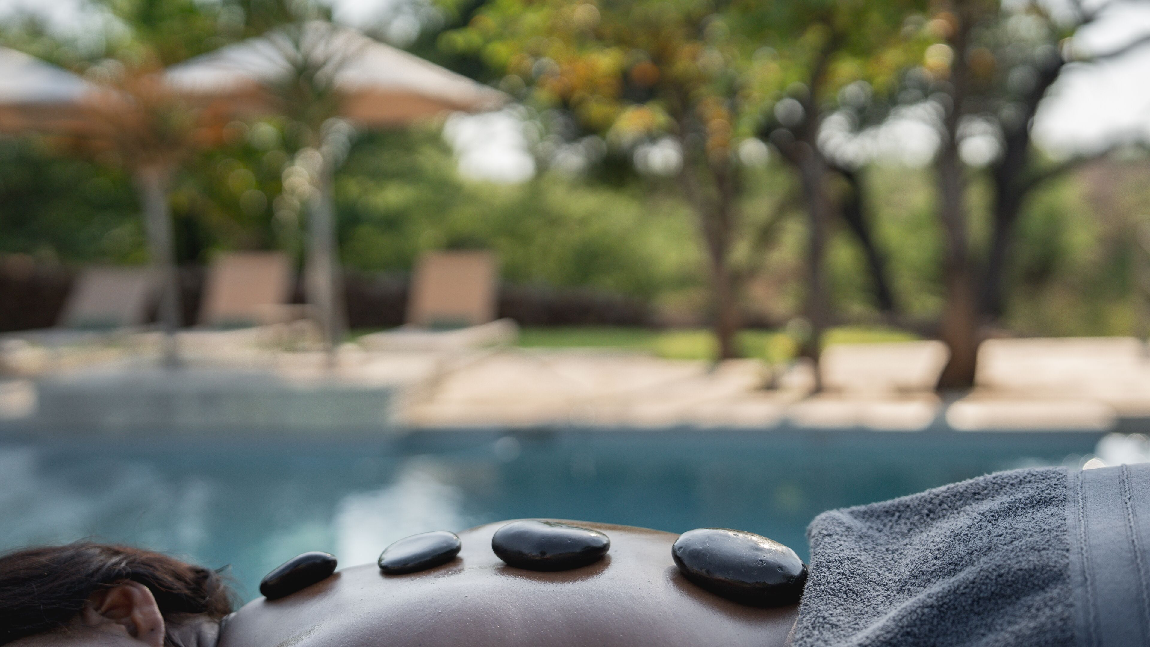 Une personne reçoit un massage aux pierres chaudes au bord d’une piscine, avec une vue dégagée sur l’eau et dans une ambiance détendue.