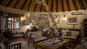 Una habitación acogedora con techo de paja, muebles de madera y varias decoraciones en las paredes, incluyendo mapas y cuadros enmarcados.