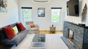 Un salon moderne comprenant un canapé, un fauteuil, une table basse, une cheminée et des œuvres d’art.