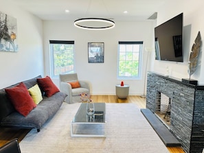 A modern living room with a sofa, armchair, coffee table, fireplace, and artwork.