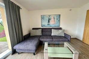 Una sala moderna con un sofá seccional, una mesa de centro de vidrio y un cuadro en la pared.