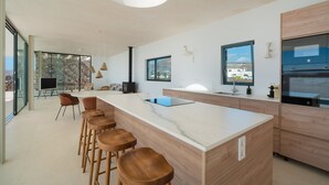 A modern kitchen with a large island, bar stools, and a stone wall backdrop.