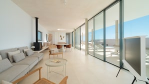 A modern living room with a sofa, coffee table, and chairs, large windows with a view, and a fireplace.