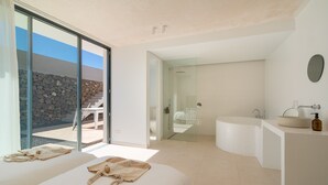 A modern bedroom with a large bed, a bathroom with a bathtub, and a glass door leading to an outdoor area.