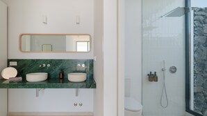 A modern bathroom with a marble countertop, two sinks, a large mirror, and a glass-enclosed shower.