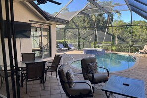 A covered outdoor area with a pool, lounge chairs, and a hot tub.