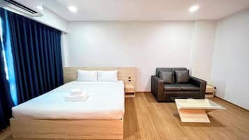 A hotel room with a large bed, a sofa, a small table, and a window with curtains.