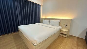 A modern hotel room with a large bed, wooden flooring, a nightstand, and a wall-mounted air conditioner.