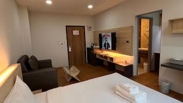 A hotel room with a bed, a desk, a TV, and a bathroom visible through an open door.
