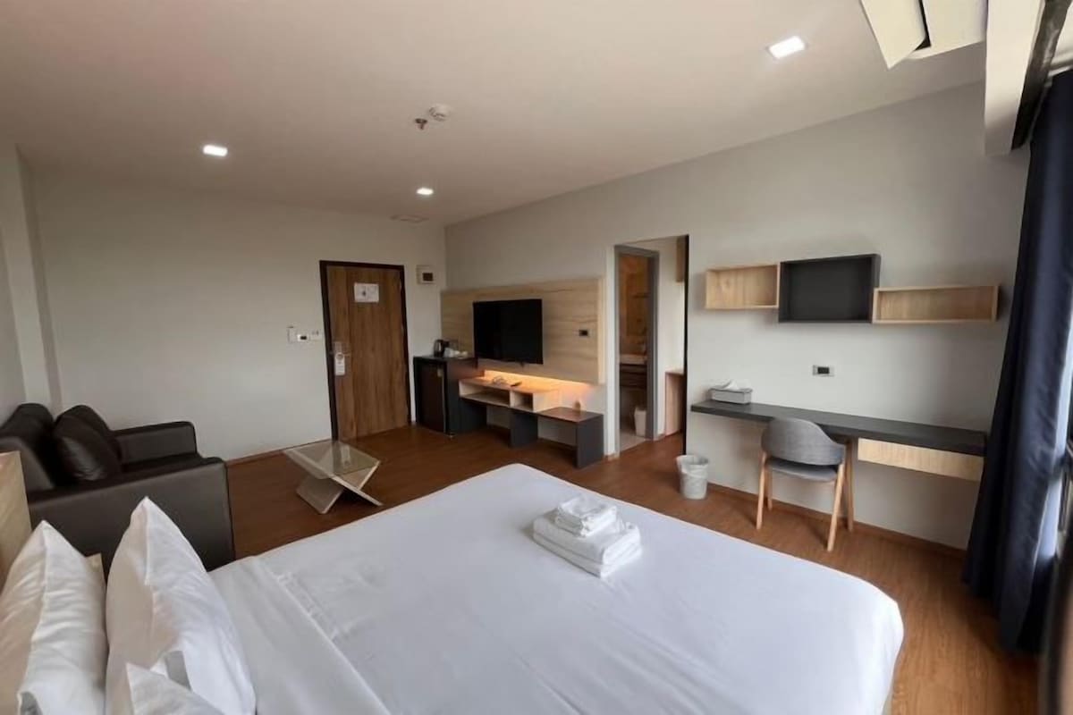 A hotel room with a large bed, a desk, a chair, a TV, and a small kitchenette.