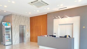 A modern reception area with a marble wall, a wooden panel, a reception desk, and a vending machine. - JIA HAUS Hotel Apartment (Buriram)