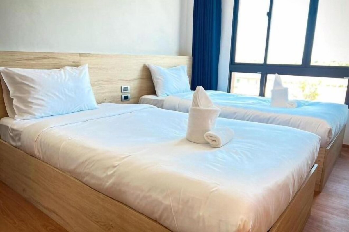 A hotel room with two beds, each with white linens and a rolled towel on the bed.