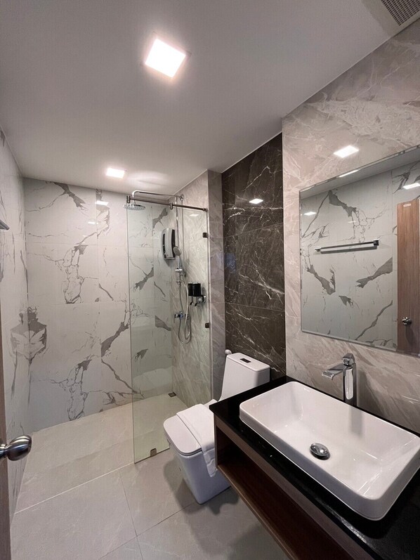 Un baño moderno con ducha acristalada, un lavamanos blanco y paredes de mármol.