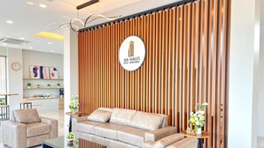 A modern hotel lobby with a sofa set, a coffee table, and a decorative wall with vertical wooden slats. - JIA HAUS Hotel Apartment (Buriram)