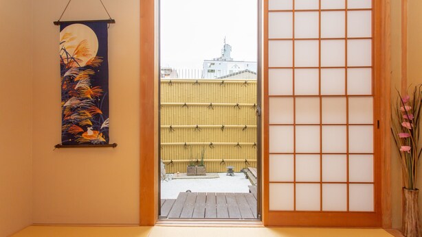 Ett traditionellt japanskt rum med tatamimattor på golvet, en skjutdörr av rispapper och en upphängd rullbild på väggen.