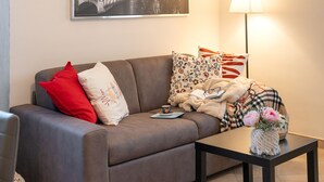 A living room with a grey sofa, a black coffee table, a lamp, and a framed cityscape picture on the wall.
