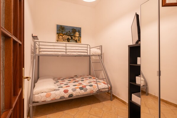 Una litera con un colchón de estampado geométrico colorido, una escalera y un cuadro de una escena de playa en la pared.