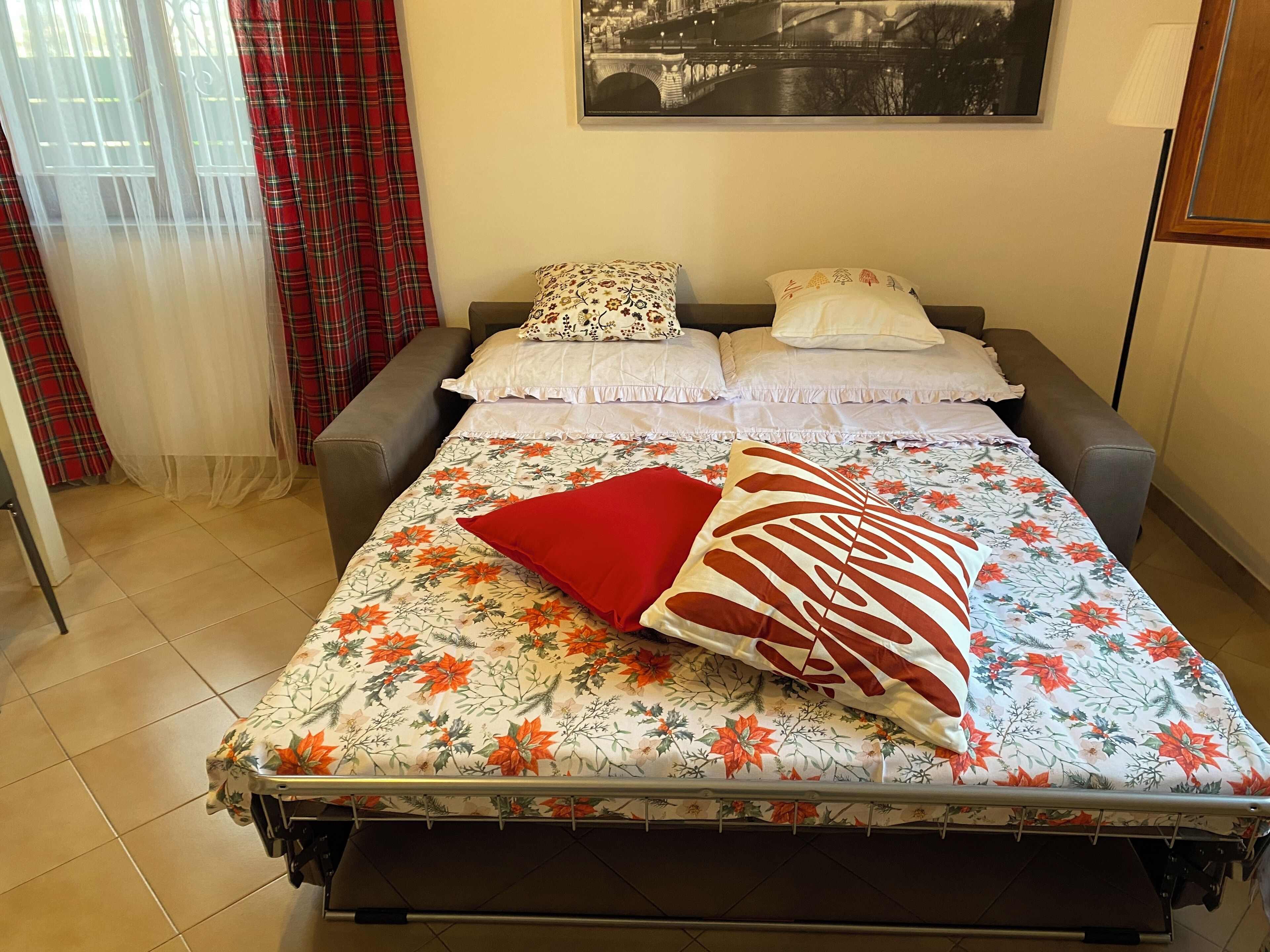 Ein Bett mit blumigem Bettzeug, zwei Kissen und ein rotes Kissen.