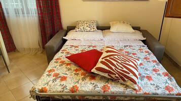 Ein Bett mit blumigem Bettzeug, zwei Kissen und ein rotes Kissen.