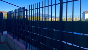A metal fence with vertical bars and a concrete base, overlooking a residential area with houses and a mountain in the background.