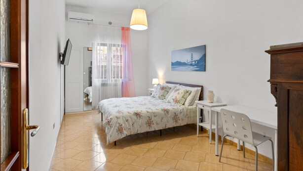 A bedroom with a bed, bedside table, lamp, and a desk with a chair.