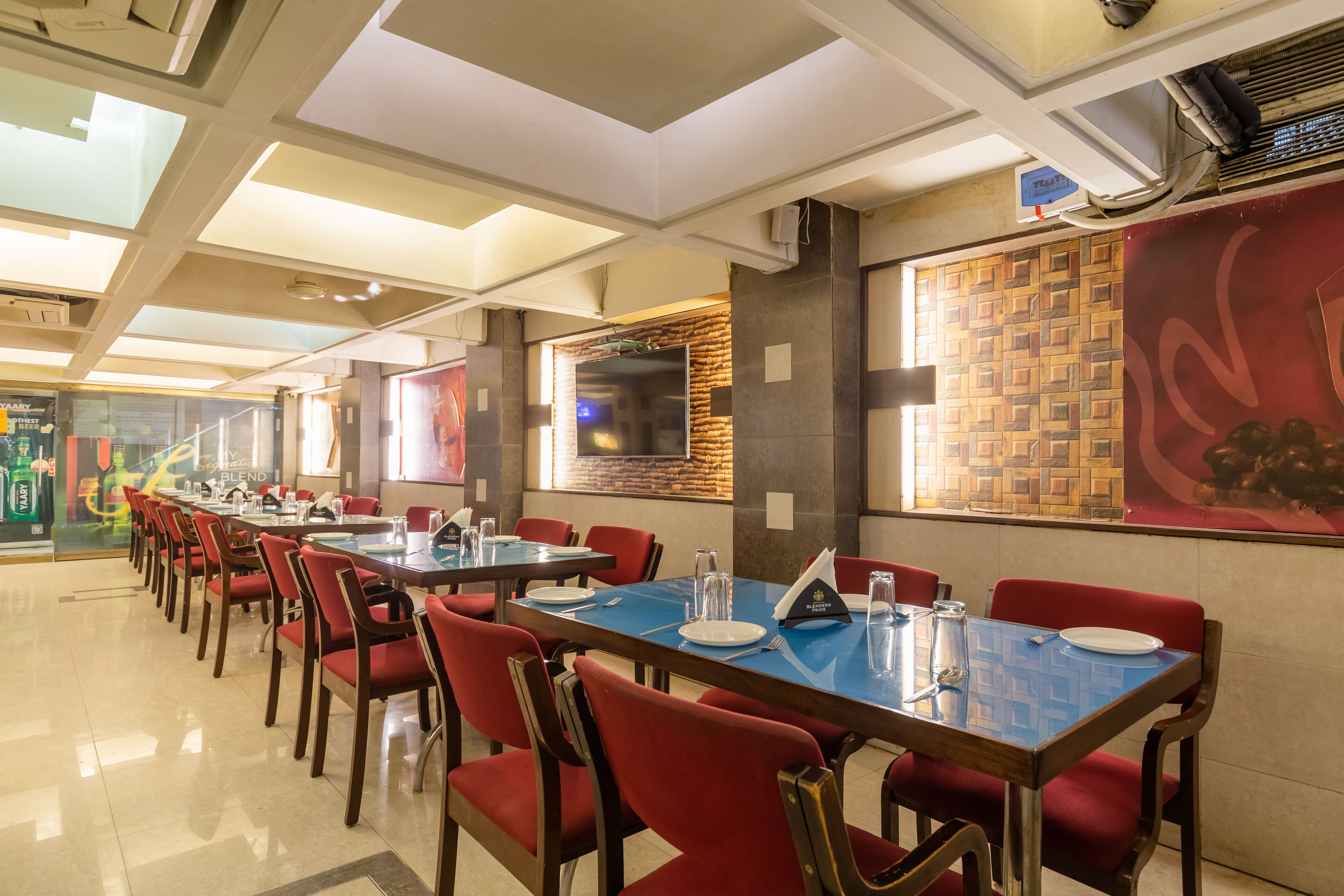 A restaurant with long tables and red chairs, a tiled floor, and a wall with a patterned design.