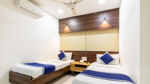 A hotel room with two single beds, a wooden headboard, a ceiling fan, and a wall-mounted air conditioner. - HOTEL KALINGA (Indore)