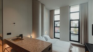 A modern hotel room with a large bed, a built-in granite sink, and large windows offering a city view. - PlexiSpace (Athens)