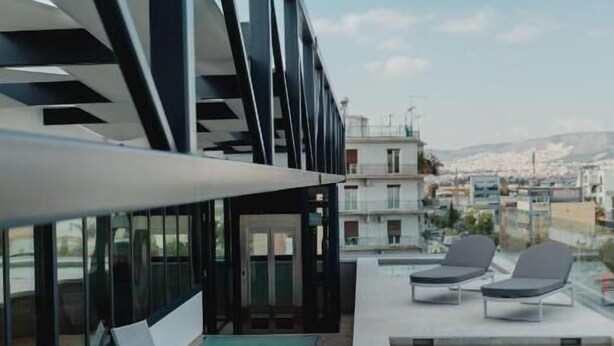 A rooftop pool area with lounge chairs, a glass-enclosed structure, and a view of the cityscape. - PlexiSpace (Athens)