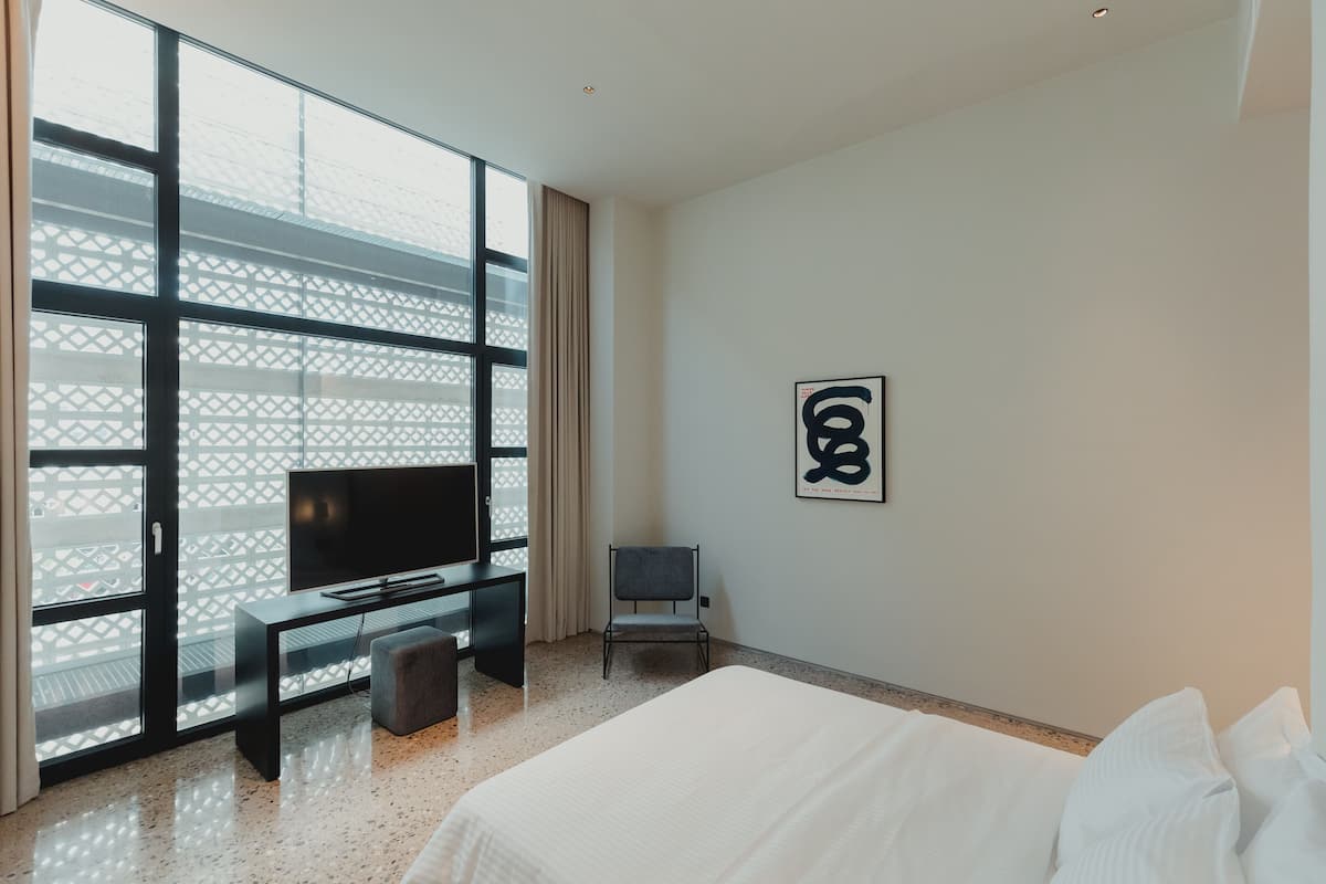 A modern hotel room with a large bed, a TV, a desk, and a chair.