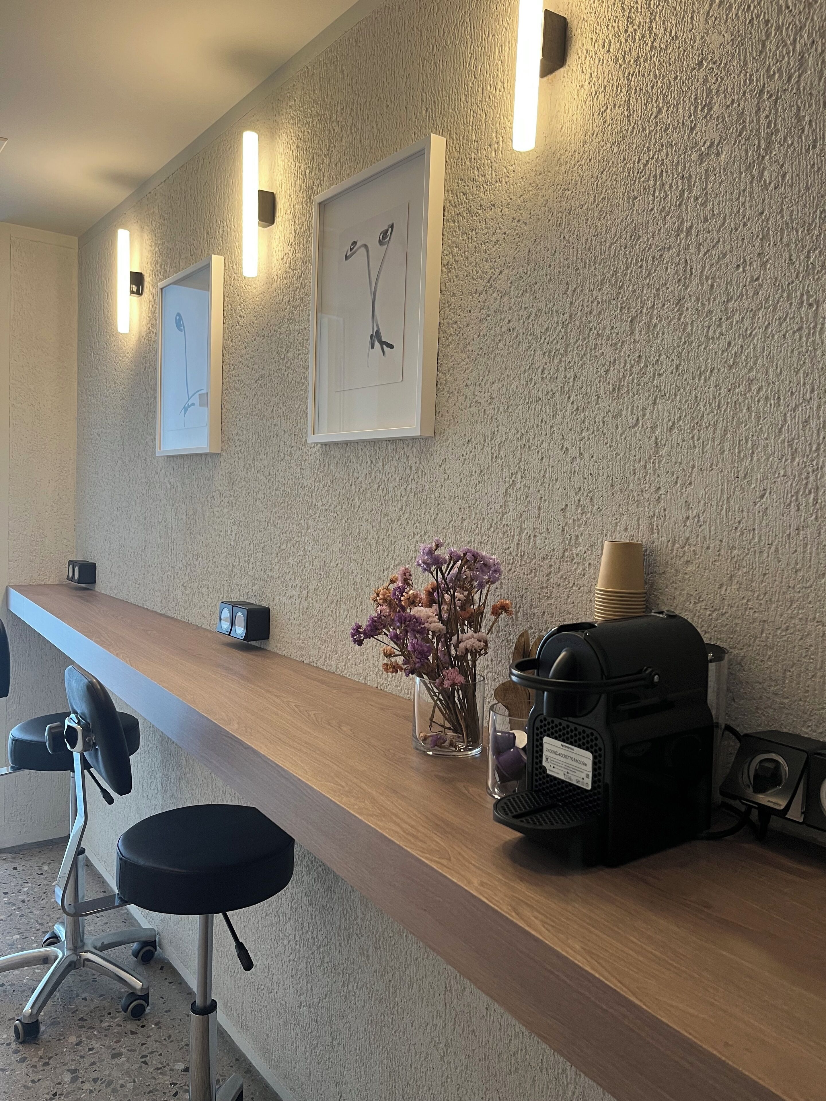 Un mostrador de recepción con encimera de madera, dos cuadros enmarcados, un florero con flores, una cafetera y un altavoz.