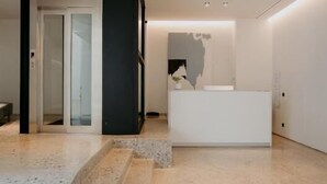 A modern reception area with a white reception desk, a glass door entrance, and a curved stone floor. - PlexiSpace (Athens)