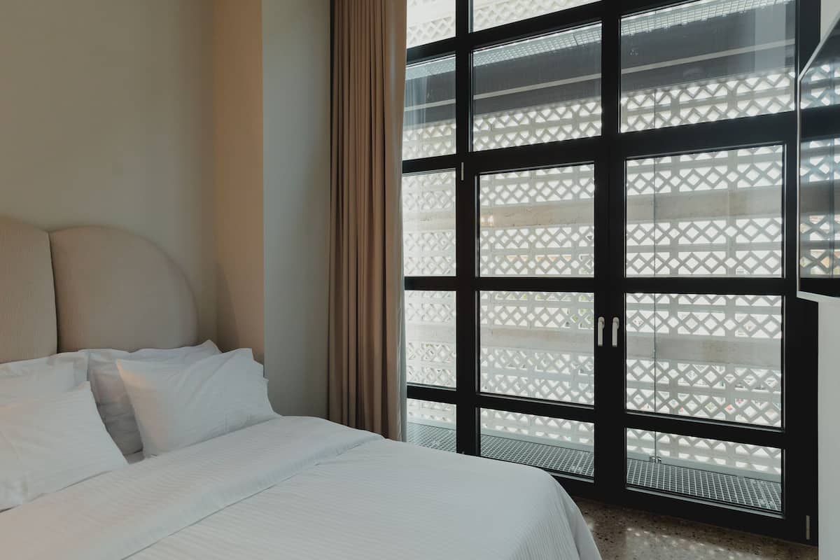 A hotel room with a bed, a window with a lattice design, and a view of the outside.