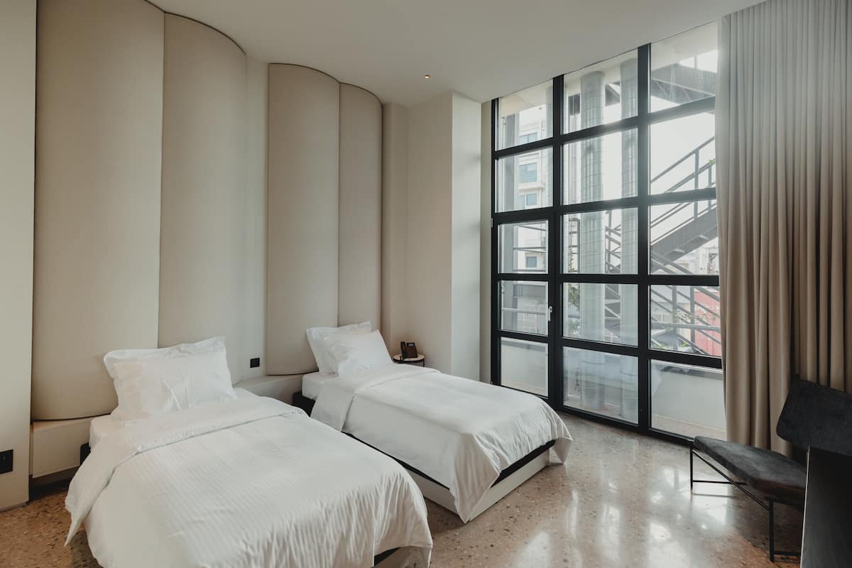 A modern hotel room with two beds, a large window with a city view, and a curved wall design.