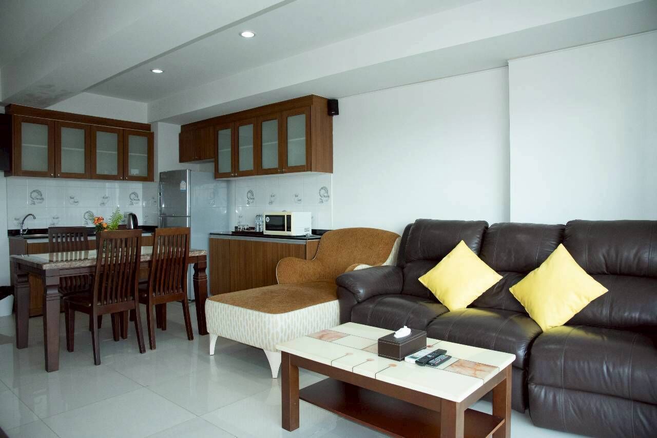 Una cocina moderna con armarios de madera, un comedor con mesa y sillas, y una sala de estar con sofá de cuero y cojines.
