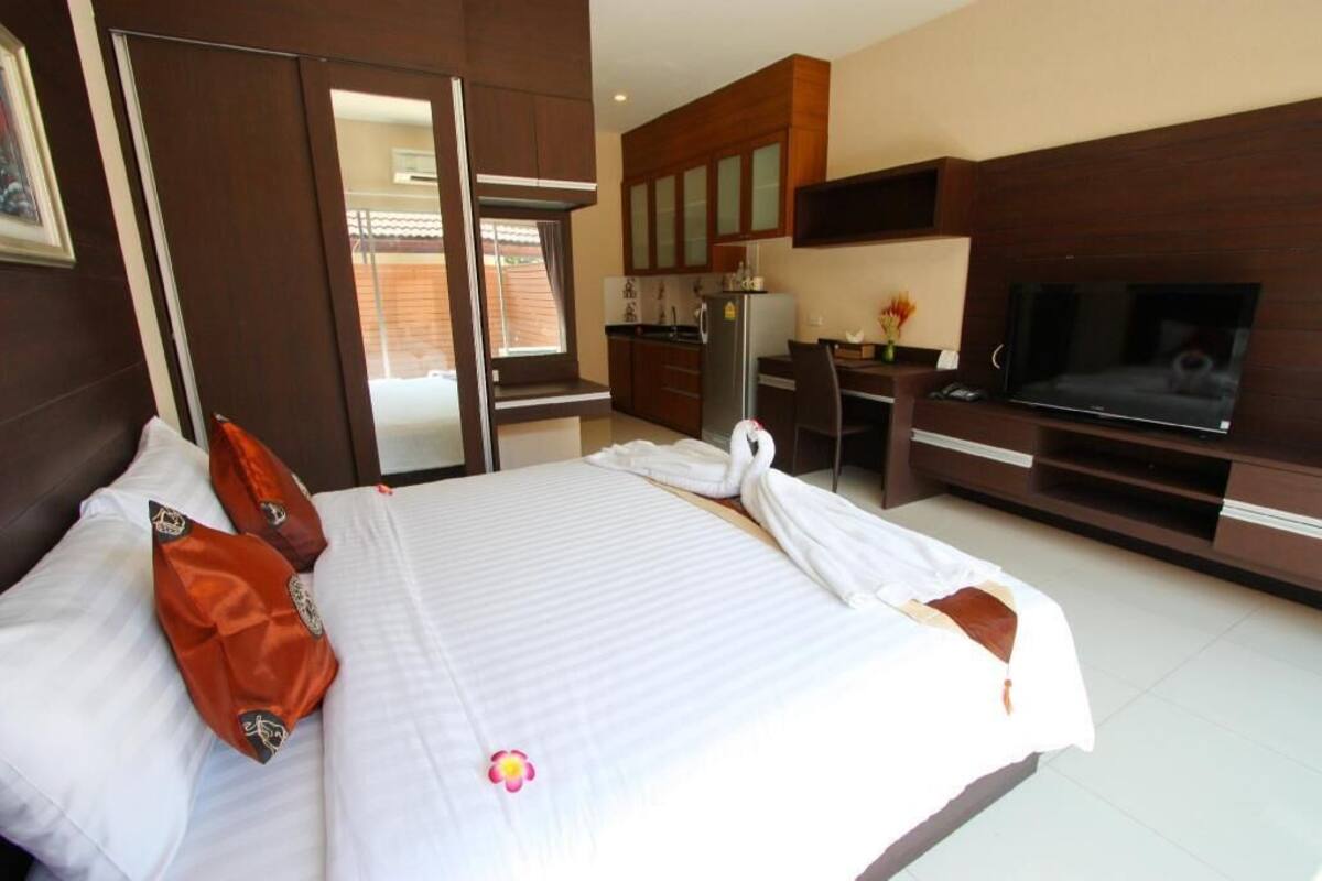 A hotel room with a bed, a TV, a desk, and a kitchenette.