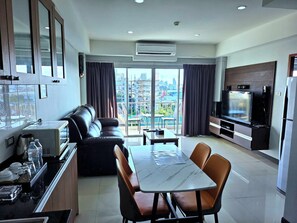 A modern living room with a sofa, a dining table with chairs, a TV, and a kitchen area with cabinets and a refrigerator. - Valhalla Pattaya Hotel (Pattaya)