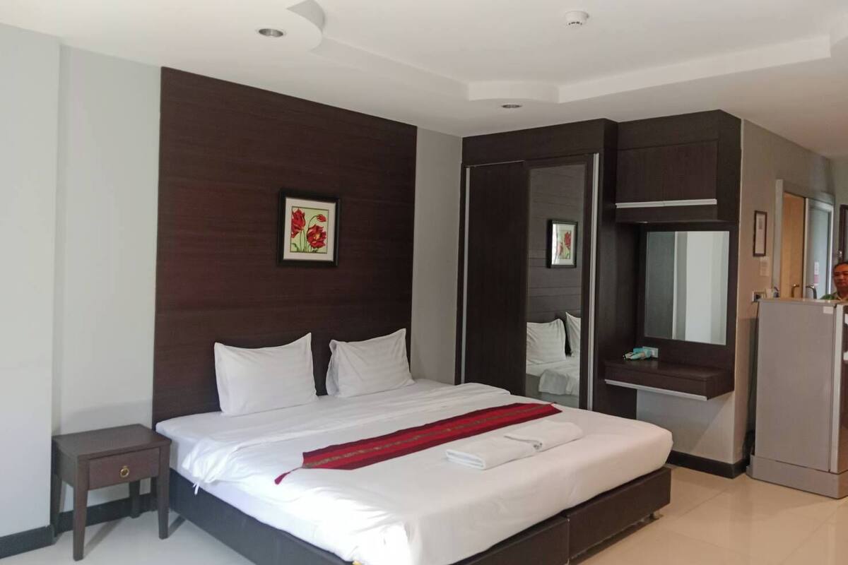 A modern hotel room with a large bed, a small bedside table, a wardrobe, and a mirror.