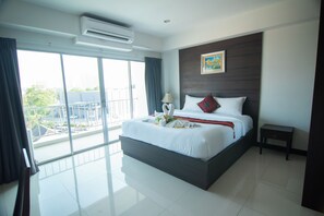 A modern hotel room with a large bed, a small bedside table, a nightstand, a window with curtains, and an air conditioning unit.