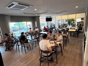 Un comedor con varias mesas y sillas, ventanas amplias y un televisor de pantalla plana en la pared.