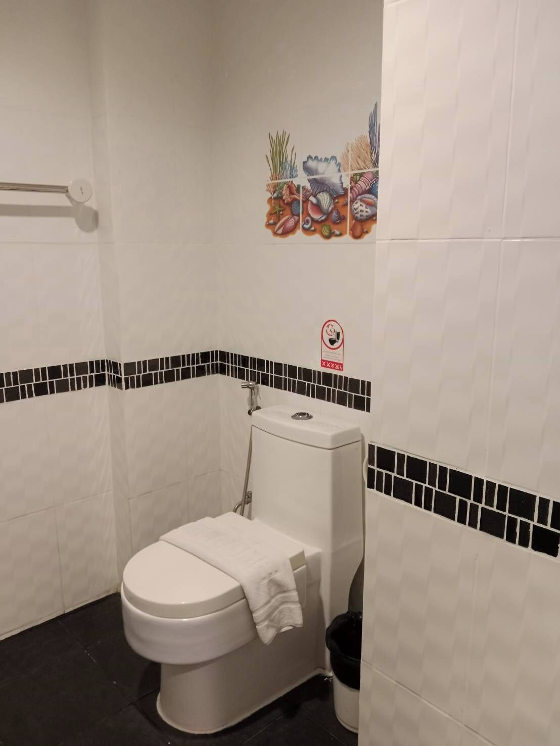 A small bathroom with a toilet, a black trash bin, and a shower area.