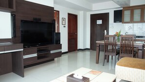 A living room with a flat-screen TV, wooden entertainment unit, dining table with chairs, and a kitchen area with cabinets. - Valhalla Pattaya Hotel (Pattaya)