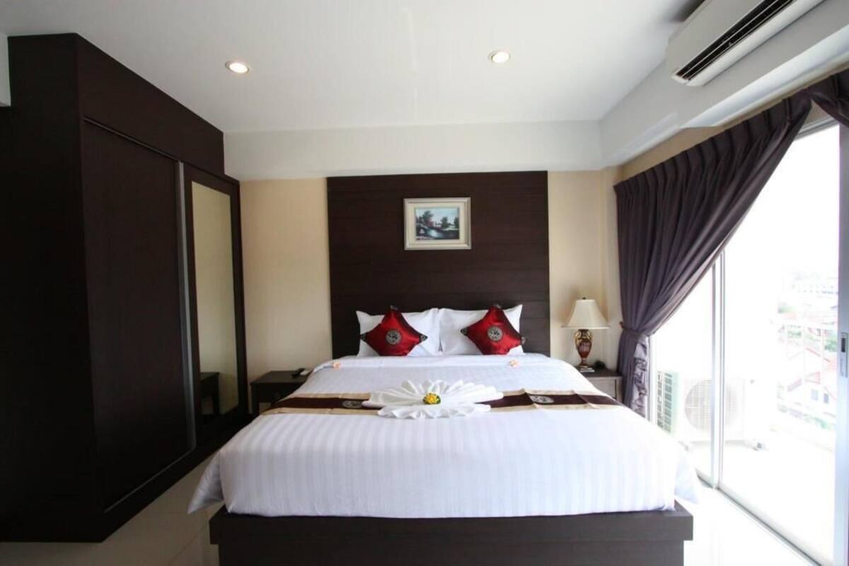 A hotel room with a large bed, a bedside table with a lamp, a window with curtains, and a picture on the wall.