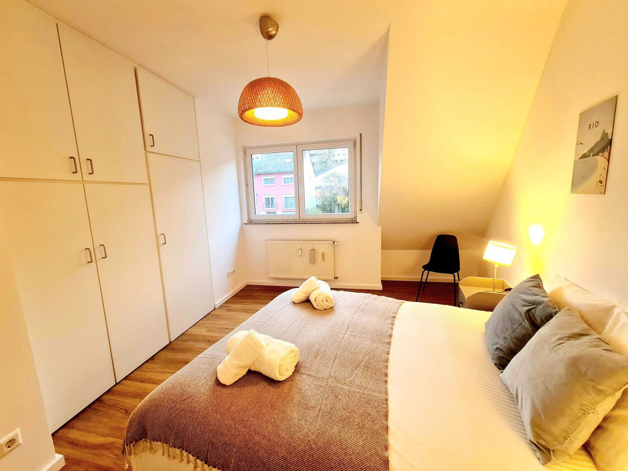 A bedroom with a bed, a window, a radiator, a chair, and a lamp.