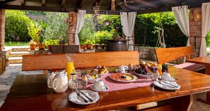 An outdoor breakfast setup with a wooden table, various breakfast items, and a garden view.