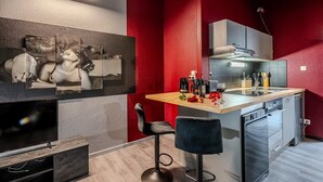 Une cuisine moderne avec un mur d’accent rouge, un îlot central doté de tabourets, un four encastré et un téléviseur à écran plat.