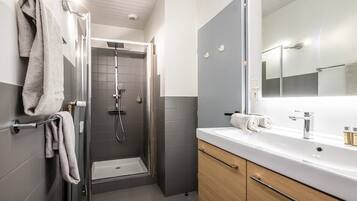 A modern bathroom with a walk-in shower, a large mirror, and a white sink.